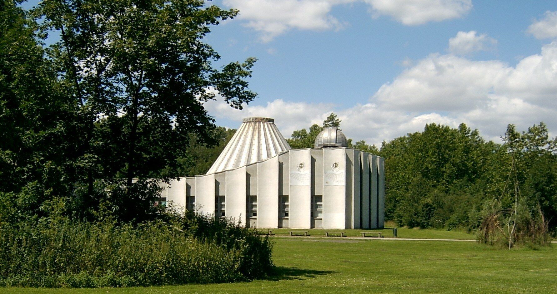 Un complejo de silos granarios con una cúpula central y dos silos cilíndricos, rodeado de vegetación y árboles.