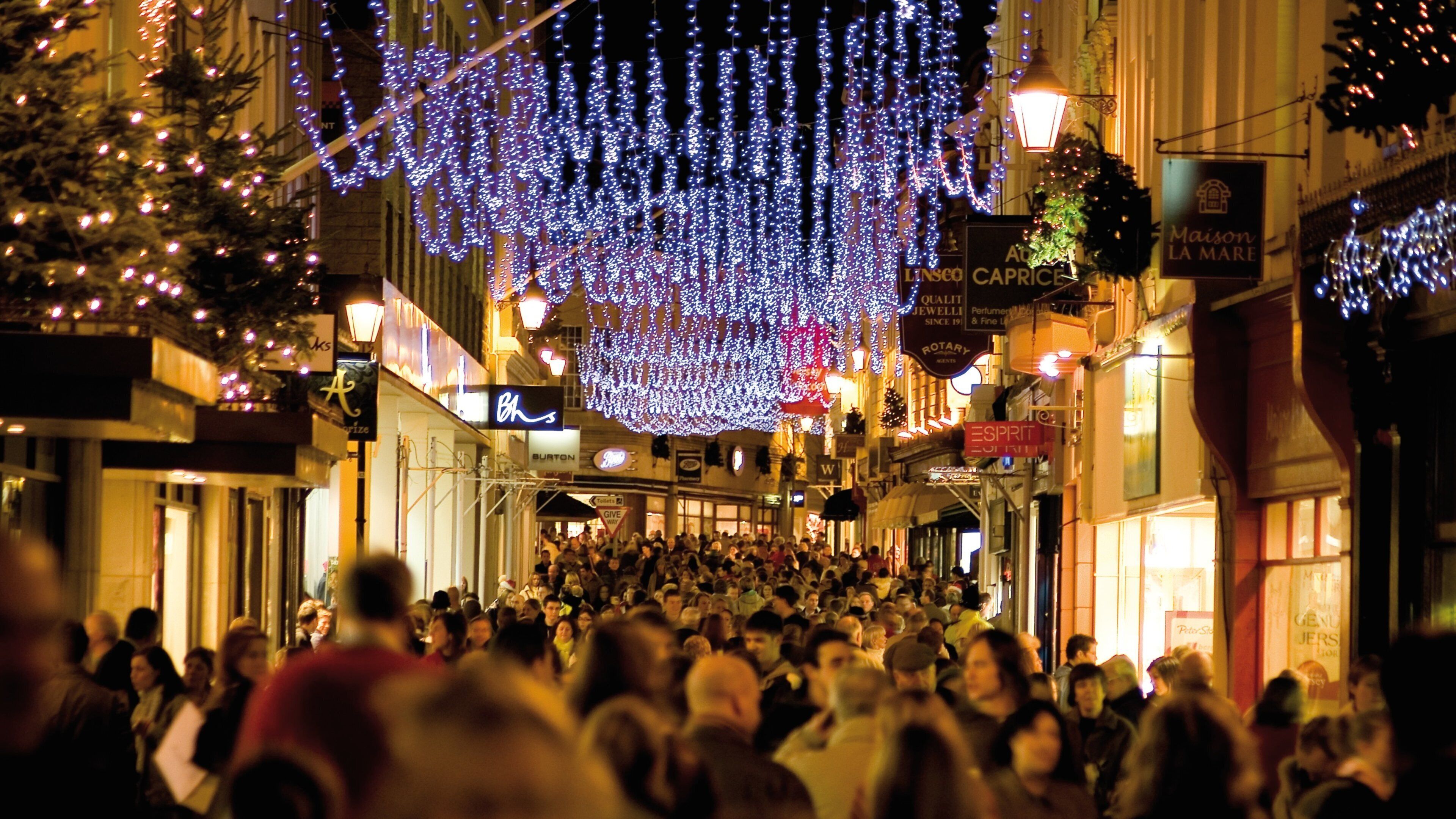 A crowded street at night with illuminated decorations and various storefronts.
