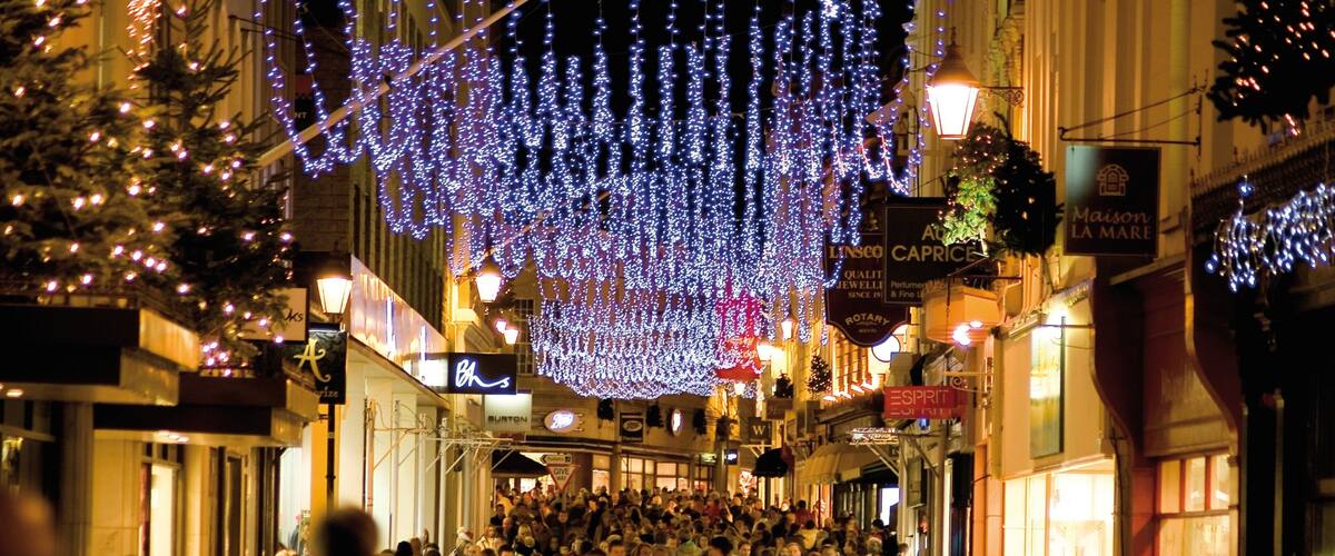 A crowded street at night with illuminated decorations and various storefronts.
