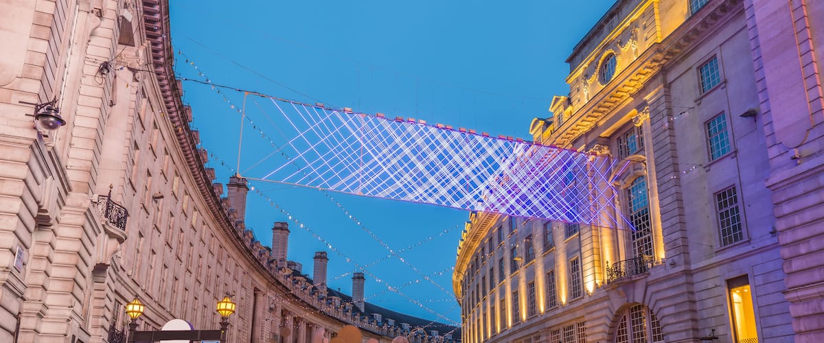 A street with historic buildings, a pedestrian bridge with lights, and a clear sky.