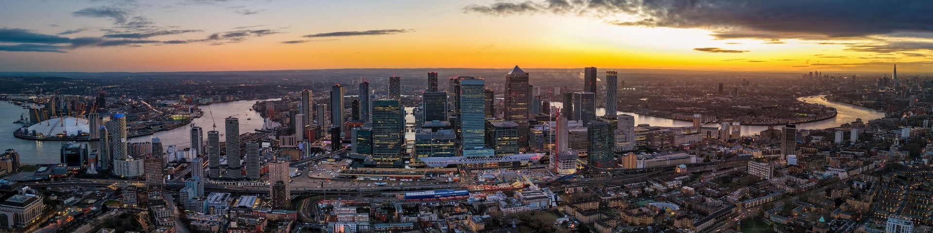 Panoramic aerial view of the iilluminated skyline of London, England, stretching from Greenwich over Canary Wharf along river Thames until Tower Bridge and the City during dusk