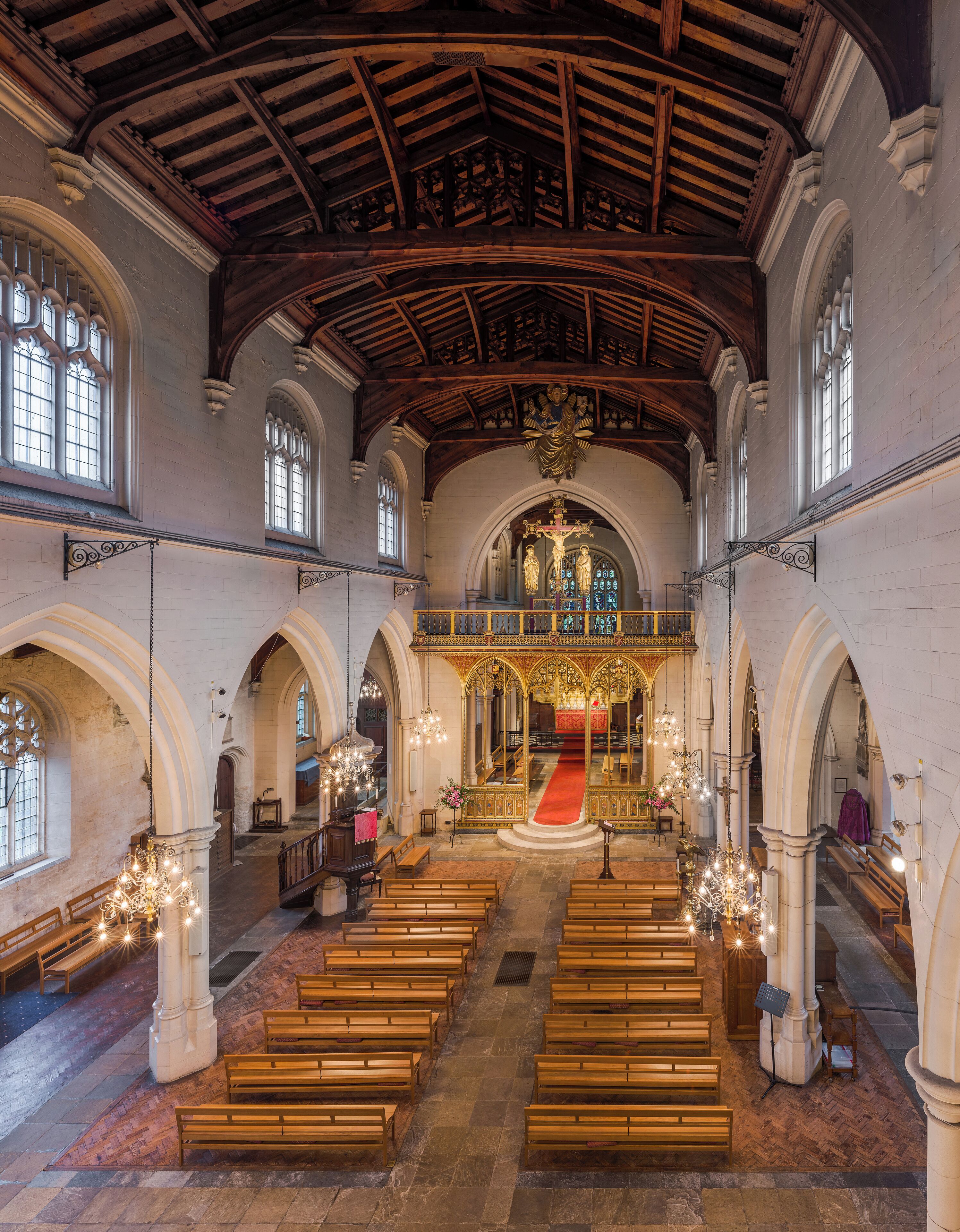 An interior of a church with wooden pews, stained glass windows, and a red carpet leading to the altar.