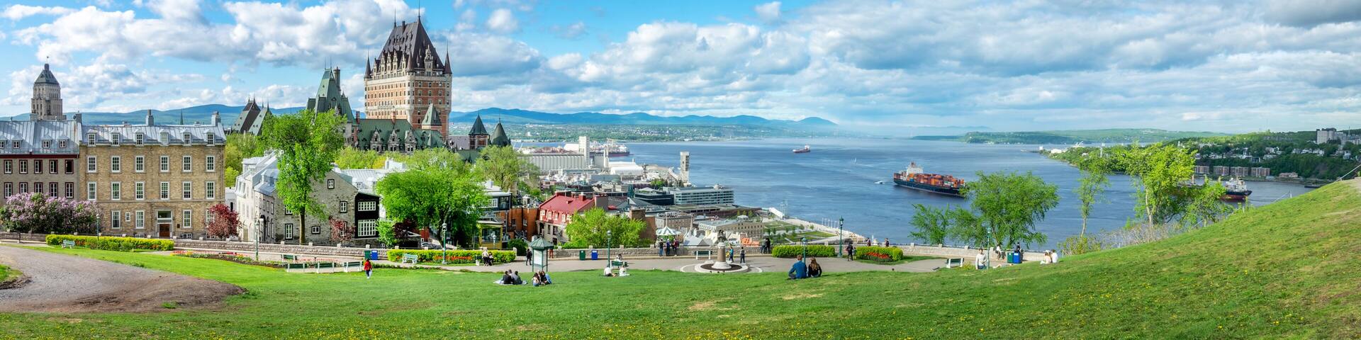 A historic building with a tower, a river with ships, and a park with people.