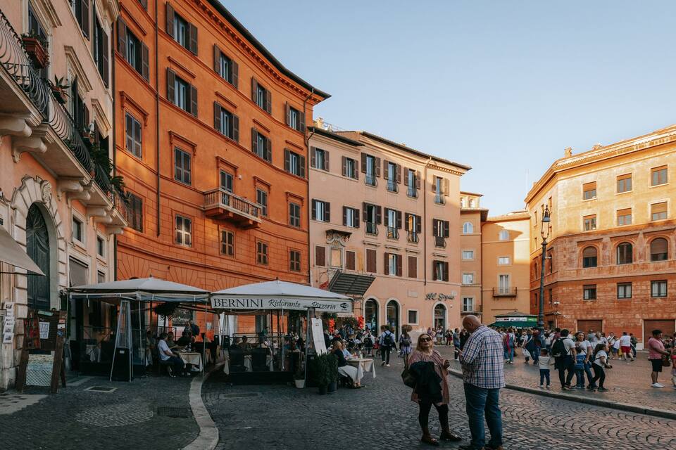 A bustling piazza with historic buildings, outdoor cafes, and people walking.