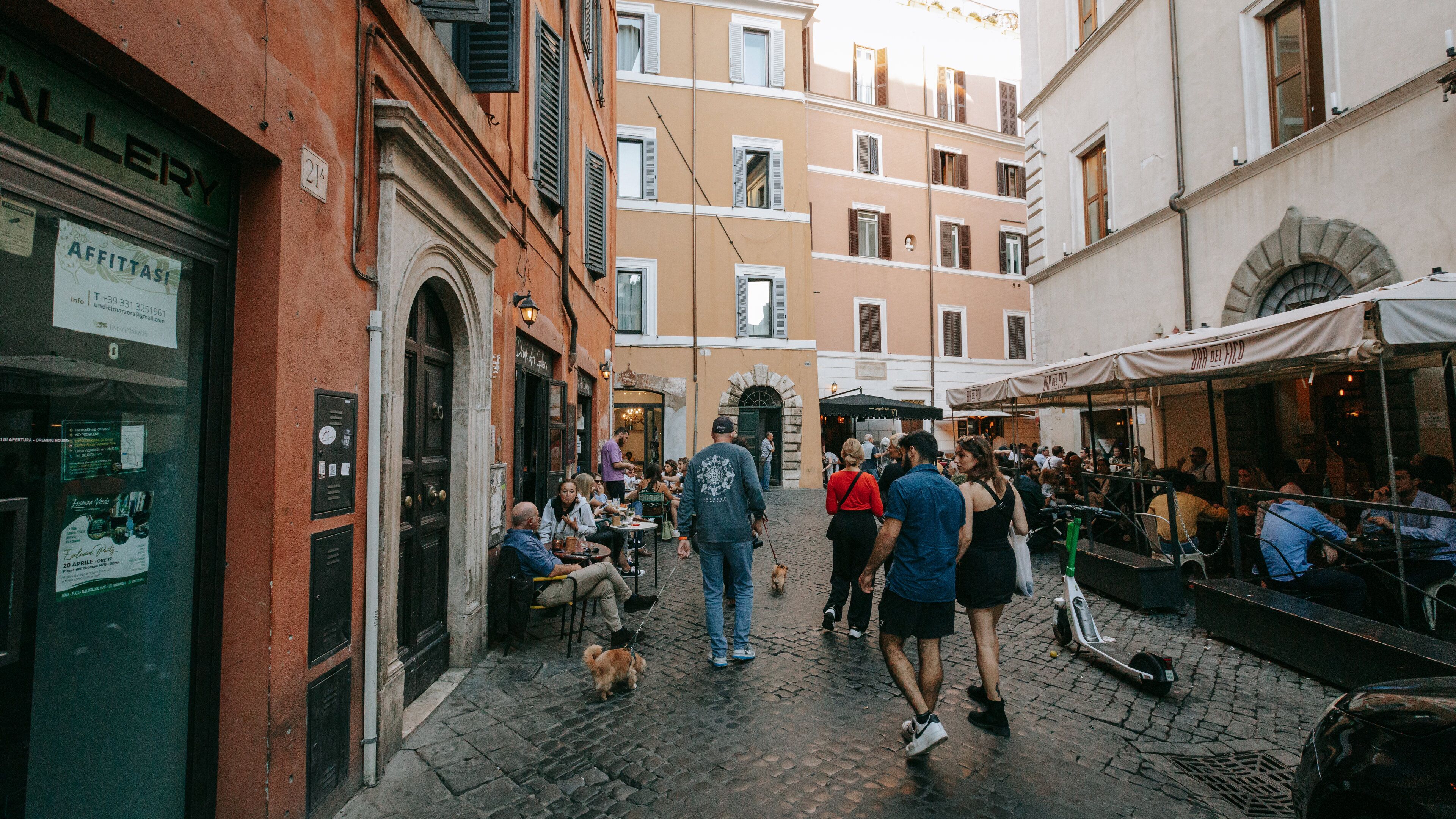 Uma rua de paralelepípedos com pessoas caminhando, cafés ao ar livre e edifícios históricos.