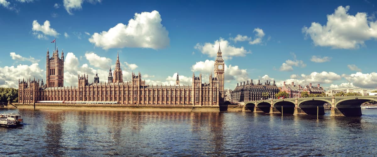 The Houses of Parliament, Big Ben, and the River Thames with a bridge and a boat.