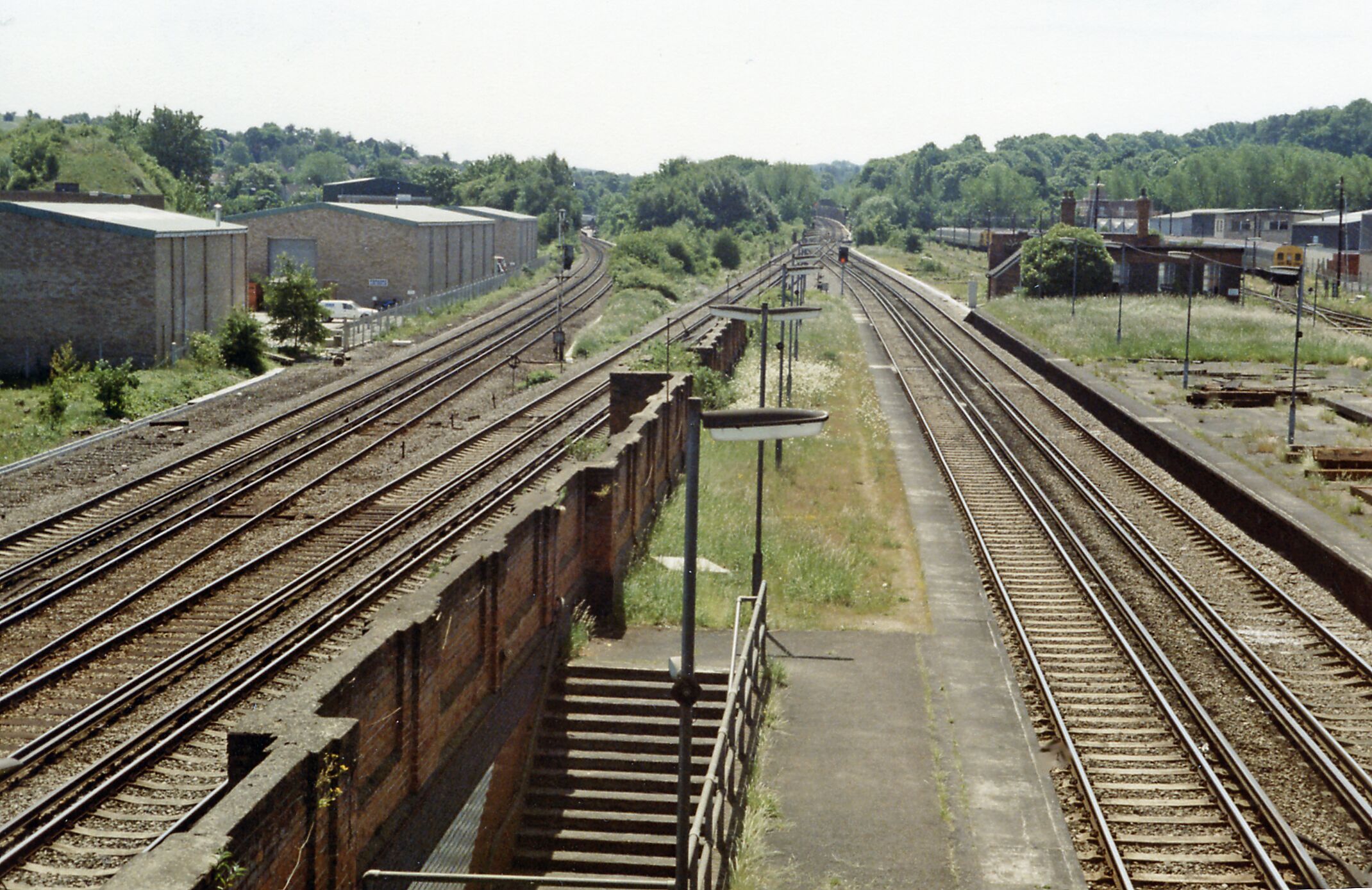 Coulsdon North: Down the lines towards Redhill and Brighton, 1983, View southwards from the footbridge at Coulsdon North station just before its final closure on 4/9/83: ex-LB&SC and SE&C lines from London (Victoria, London Bridge, Charing Cross) via East Croydon and Purley to Redhill and Brighton, etc. This station was originally 'Stoats Nest & Cane Hill', then 1911-1923 'Coulsdon & Smitham Downs'. Latterly, it was only the terminus of local trains from London and even these were run down in favour of through trains. These used the through platforms, but these tended to conflict after the quadrupling of the main line and the opening of the 'Quarry Line' (by-passing Redhill) in 1899, so most called instead at the ex-SE&CR station Coulsdon South. The two lines at far left are the original SER pair to Redhill passing through Coulsdon South - just visible. Directly on the right below are the ex-LB&SC fast lines, which join up in the distance with the middle pair of fast lines and then go straight ahead, under the Redhill lines in the Cane Hill covered way (former tunnel), to form the 'Quarry Line' by-pass. Over in the right distance are the sidings for the trains terminating at Coulsdon North. The ex-SE&C line through Smitham to Tattenham Corner is out of sight to the right. This whole area is now (2012) obscured by the A23 Coulsdon Relief roads.