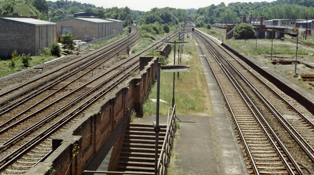Coulsdon North: Down the lines towards Redhill and Brighton, 1983, View southwards from the footbridge at Coulsdon North station just before its final closure on 4/9/83: ex-LB&SC and SE&C lines from London (Victoria, London Bridge, Charing Cross) via East Croydon and Purley to Redhill and Brighton, etc. This station was originally 'Stoats Nest & Cane Hill', then 1911-1923 'Coulsdon & Smitham Downs'. Latterly, it was only the terminus of local trains from London and even these were run down in favour of through trains. These used the through platforms, but these tended to conflict after the quadrupling of the main line and the opening of the 'Quarry Line' (by-passing Redhill) in 1899, so most called instead at the ex-SE&CR station Coulsdon South. The two lines at far left are the original SER pair to Redhill passing through Coulsdon South - just visible. Directly on the right below are the ex-LB&SC fast lines, which join up in the distance with the middle pair of fast lines and then go straight ahead, under the Redhill lines in the Cane Hill covered way (former tunnel), to form the 'Quarry Line' by-pass. Over in the right distance are the sidings for the trains terminating at Coulsdon North. The ex-SE&C line through Smitham to Tattenham Corner is out of sight to the right. This whole area is now (2012) obscured by the A23 Coulsdon Relief roads.