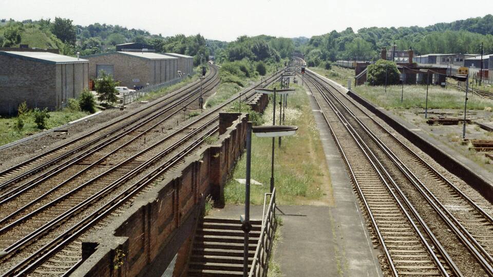 Coulsdon North: Down the lines towards Redhill and Brighton, 1983, View southwards from the footbridge at Coulsdon North station just before its final closure on 4/9/83: ex-LB&SC and SE&C lines from London (Victoria, London Bridge, Charing Cross) via East Croydon and Purley to Redhill and Brighton, etc. This station was originally 'Stoats Nest & Cane Hill', then 1911-1923 'Coulsdon & Smitham Downs'. Latterly, it was only the terminus of local trains from London and even these were run down in favour of through trains. These used the through platforms, but these tended to conflict after the quadrupling of the main line and the opening of the 'Quarry Line' (by-passing Redhill) in 1899, so most called instead at the ex-SE&CR station Coulsdon South. The two lines at far left are the original SER pair to Redhill passing through Coulsdon South - just visible. Directly on the right below are the ex-LB&SC fast lines, which join up in the distance with the middle pair of fast lines and then go straight ahead, under the Redhill lines in the Cane Hill covered way (former tunnel), to form the 'Quarry Line' by-pass. Over in the right distance are the sidings for the trains terminating at Coulsdon North. The ex-SE&C line through Smitham to Tattenham Corner is out of sight to the right. This whole area is now (2012) obscured by the A23 Coulsdon Relief roads.