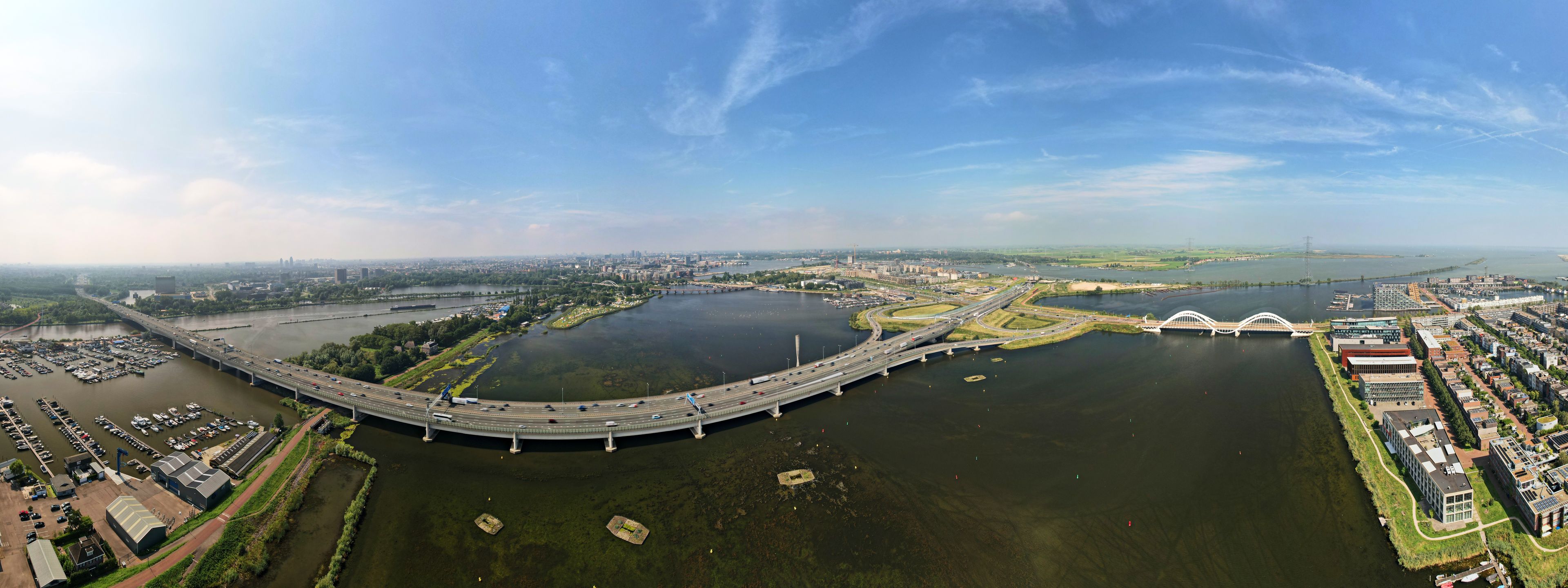 Un río con un puente, un puerto deportivo y un paisaje urbano al fondo.