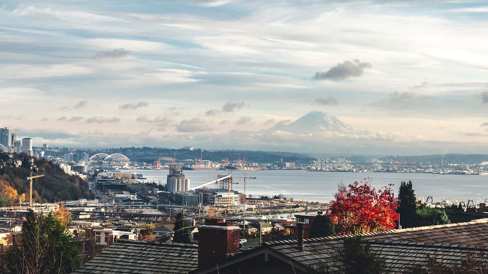 A cityscape with a prominent mountain in the background, a body of water, and a mix of urban and natural landscapes.
