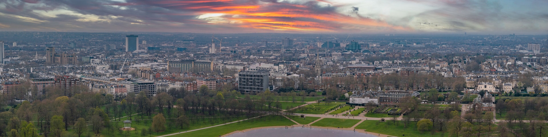 Une vue sur une ville avec un grand parc, un lac et un ciel au coucher du soleil.