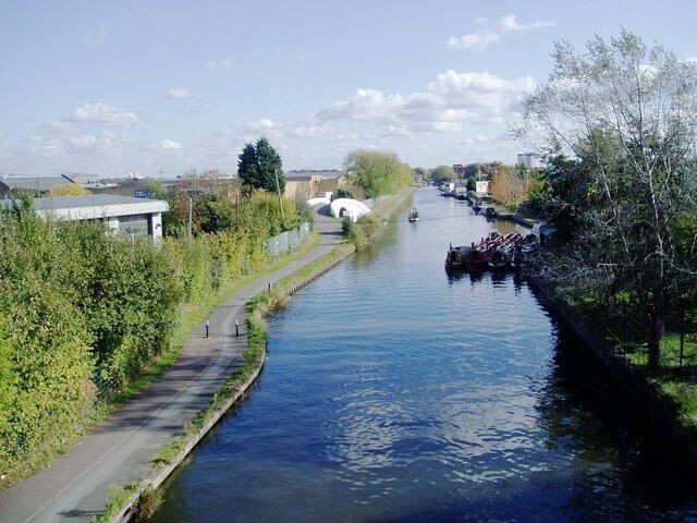 Grand Union canal showing the Bulls Bridge. View from The Parkway looking east. The Bulls Bridge is the white structure on the left of the canal in the middle distance. Tesco supermarket is to the right (unseen). The partially revealed square structure on the left is part of the Volvo truck servicing centre.