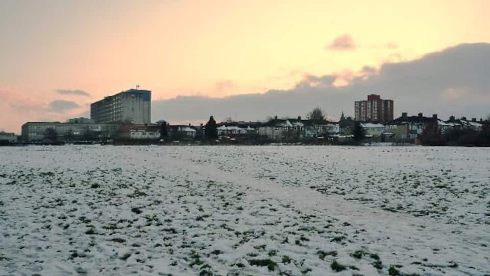 A snow-covered field with buildings in the background during sunset.