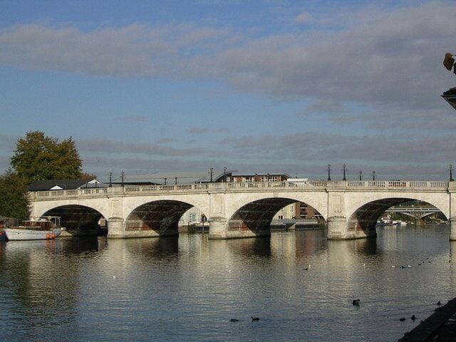 Un puente de piedra con tres arcos sobre un río tranquilo.