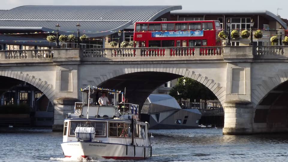 Kingston Bridge. Busy scene at Kingston-upon-Thames with a double-deck London bus on the 1828 bridge (widened in 1914 and 2001) and a pleasure boat heading upstream on the river. http://www.kingston.gov.uk/