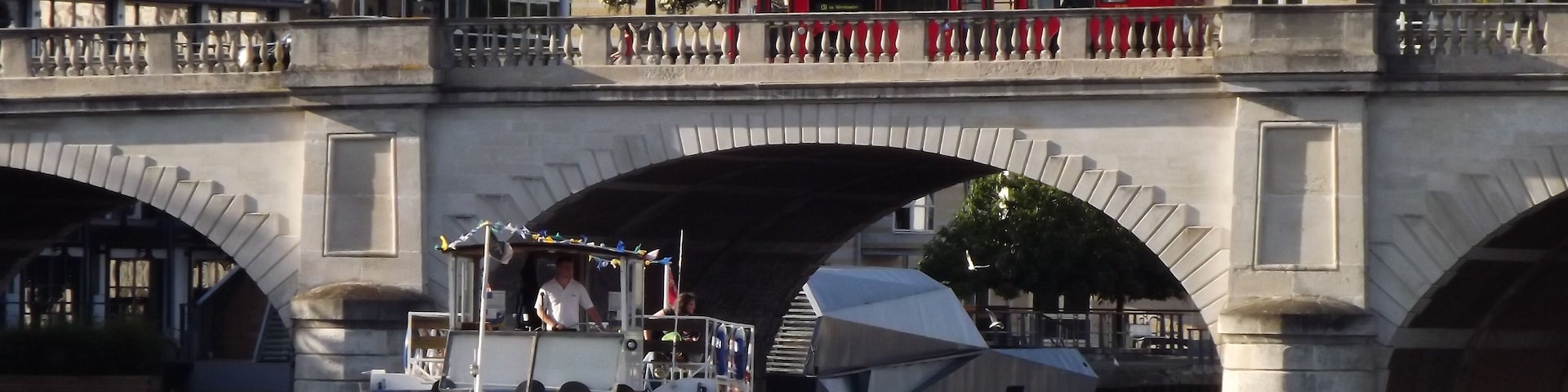 Kingston Bridge. Busy scene at Kingston-upon-Thames with a double-deck London bus on the 1828 bridge (widened in 1914 and 2001) and a pleasure boat heading upstream on the river. http://www.kingston.gov.uk/