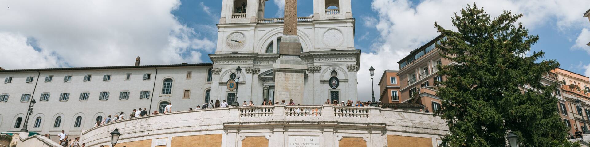 A grand staircase leading to a historic building with two towers and a tall obelisk.