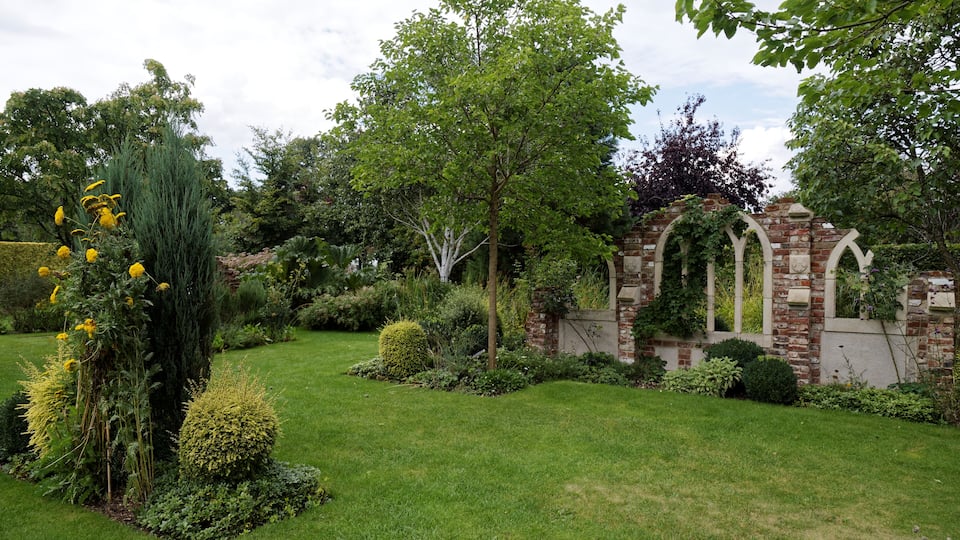 Un jardin bien entretenu, agrémenté d’une arche en briques, de divers arbustes et d’un grand conifère.