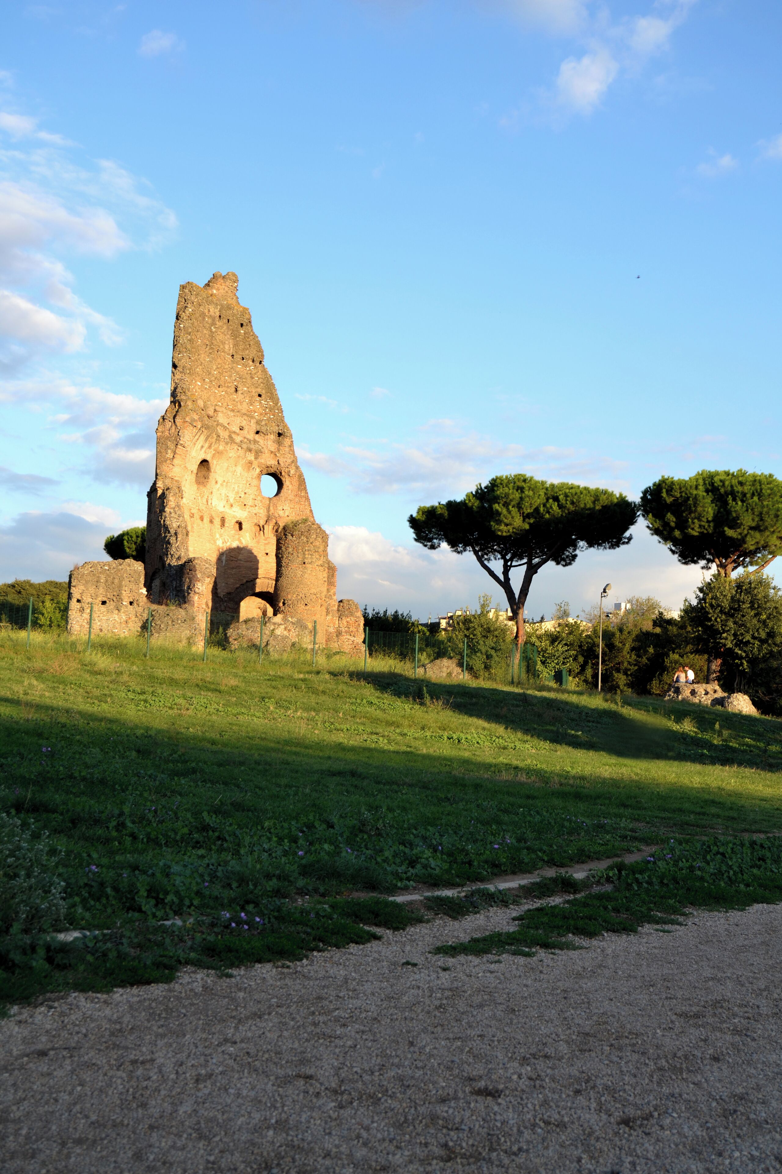 Una torre de piedra histórica con un gran agujero en el centro, rodeada de césped verde y árboles.