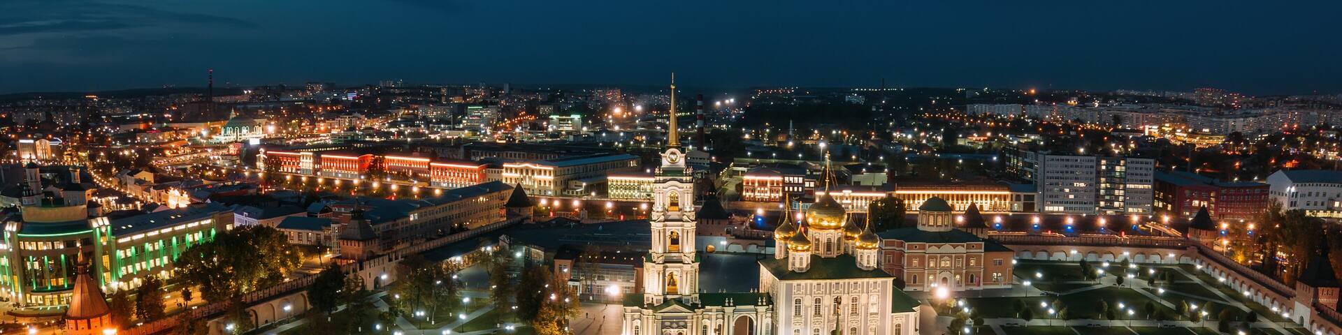 A cityscape at night with illuminated buildings, a prominent church with a tall tower, and a well-lit square.