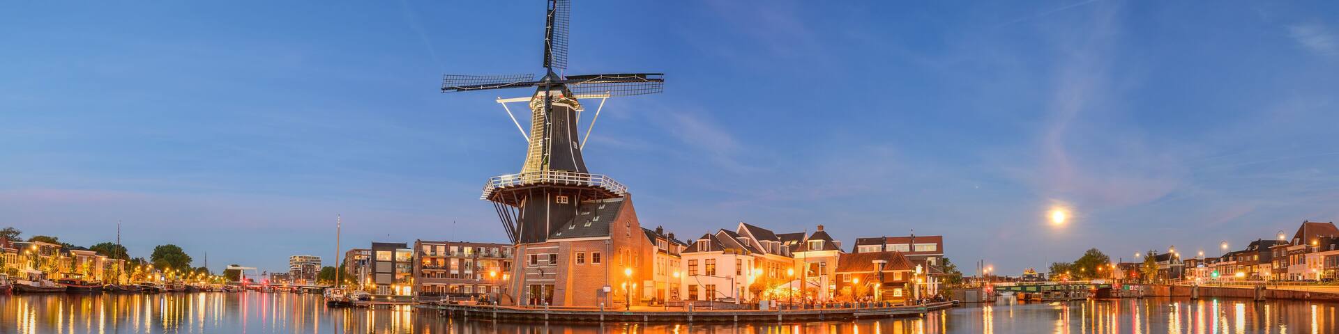 A windmill in the center of a calm river with buildings on both sides.