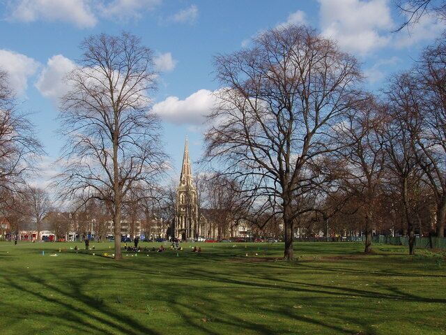 Turnham Green with leafless trees in winter, near to Chiswick, Hounslow, Great Britain. A group of children are playing just beyond the trees, and Christ Church is seen beyond the park.