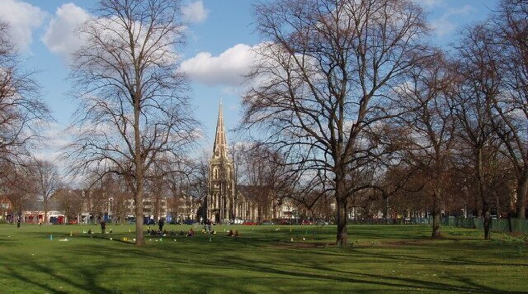 Turnham Green with leafless trees in winter, near to Chiswick, Hounslow, Great Britain. A group of children are playing just beyond the trees, and Christ Church is seen beyond the park.