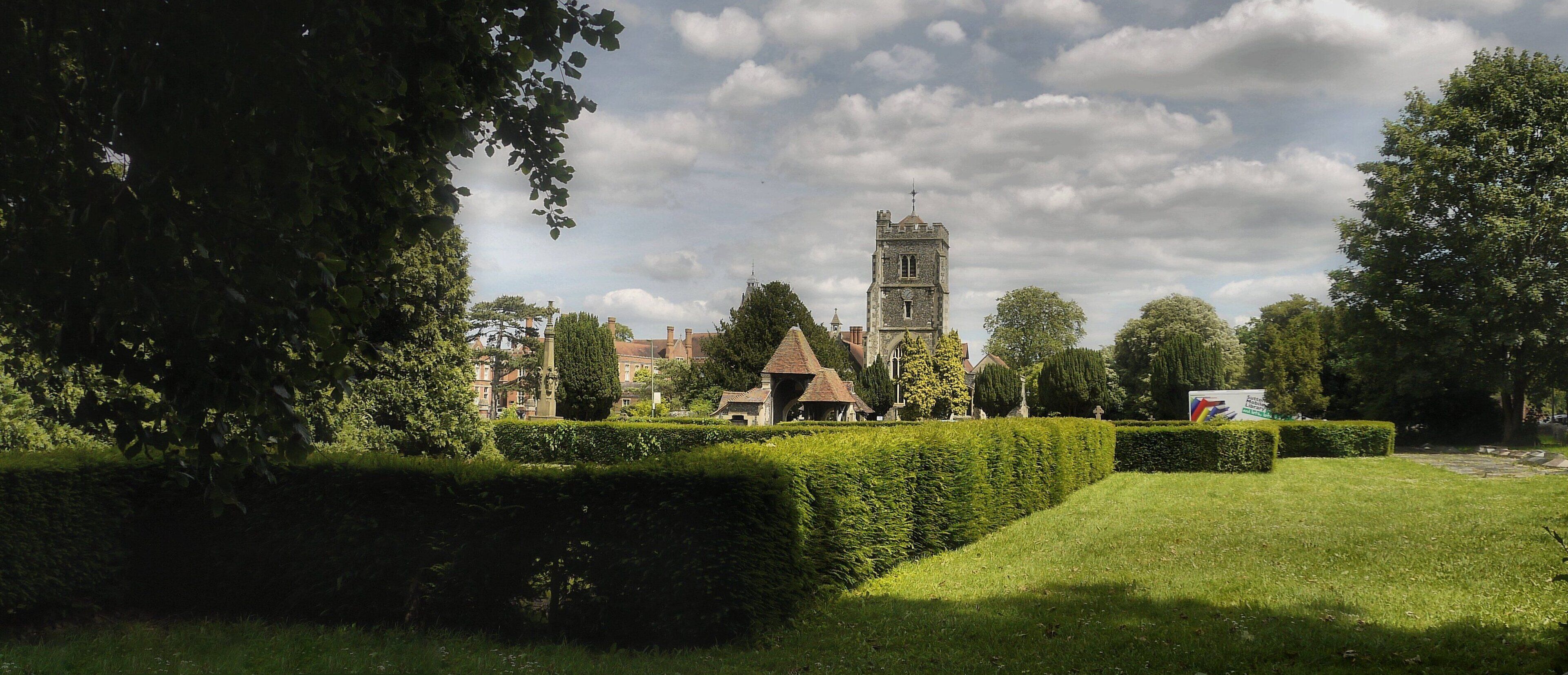 A historic tower, neatly trimmed hedges, and a grassy park area.