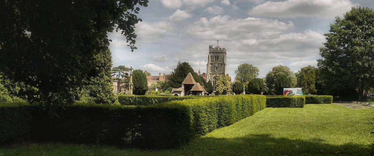 A historic tower, neatly trimmed hedges, and a grassy park area.