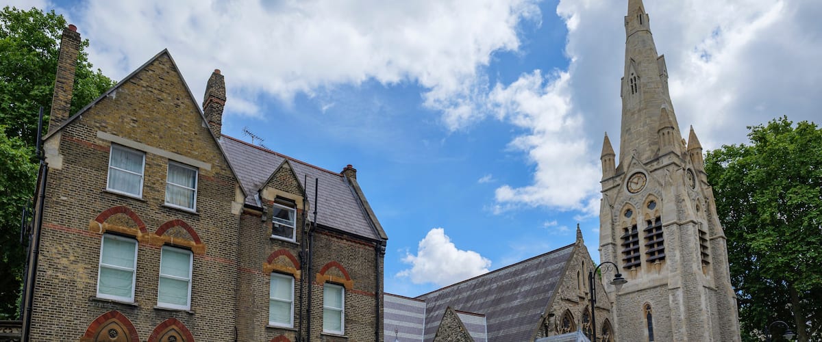 Una iglesia histórica con una aguja alta y edificios residenciales contiguos.
