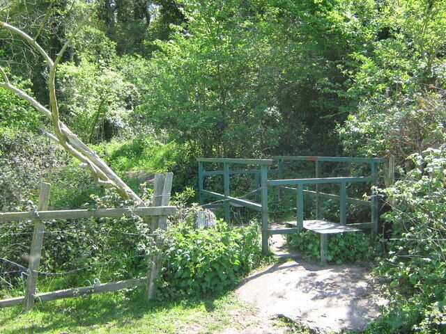 Footbridge over ditch This storm drain ditch is on the border between the London Borough of Bexley and Kent. The trees are in Dartford Heath, a large lowland common managed by Dartford Borough Council. The footbridge is on a footpath from Cold Blow Crescent to Portman Close.