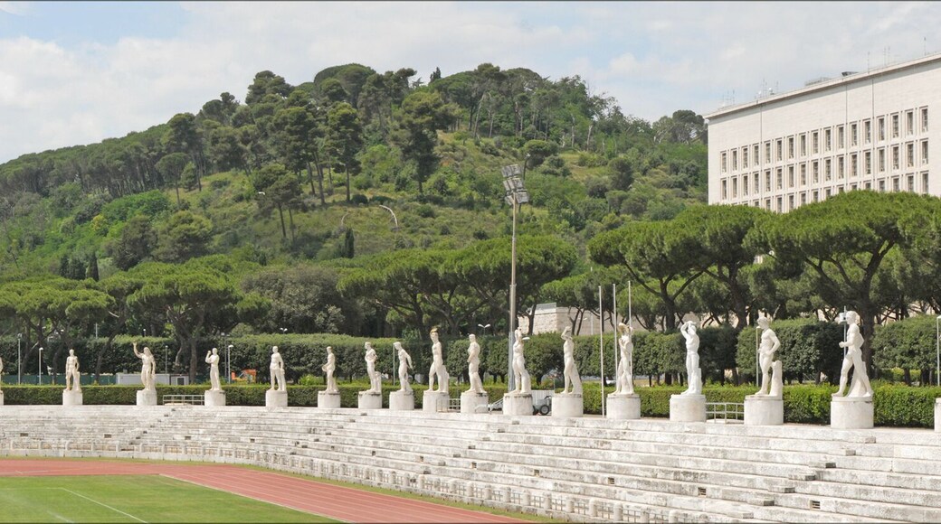 Le stade des marbres (Photo panoramique) A gauche, le stade olympique ____________ Le Foro Italico, appelé dans les années 30, Foro Mussolini, est un grand ensemble de bâtiments et d'équipements sportifs. Sa construction a débuté à l'époque fasciste sous la direction de l'architecte Enrico Del Dubbio. Le Foro a été inauguré en 1932. A l'entrée, un obélisque en marbre dédié à Mussolini a été érigé. Le stade des marbres est l'équipement le plus célèbre avec ses 60 statues d'athlètes à l'antique, placées au-dessus des gradins et offertes par les villes et provinces d'Italie. A l'entrée, se trouvait l'Académie d"éducation physique, constituée de deux corps de bâtiments rouges, symétriques et reliés par une loggia. Les locaux sont occupés aujourd'hui par le comité olympique italien. A proximité, un stade olympique a été construit pour les jeux de 1960 puis agrandi pour la coupe du monde de 1990.