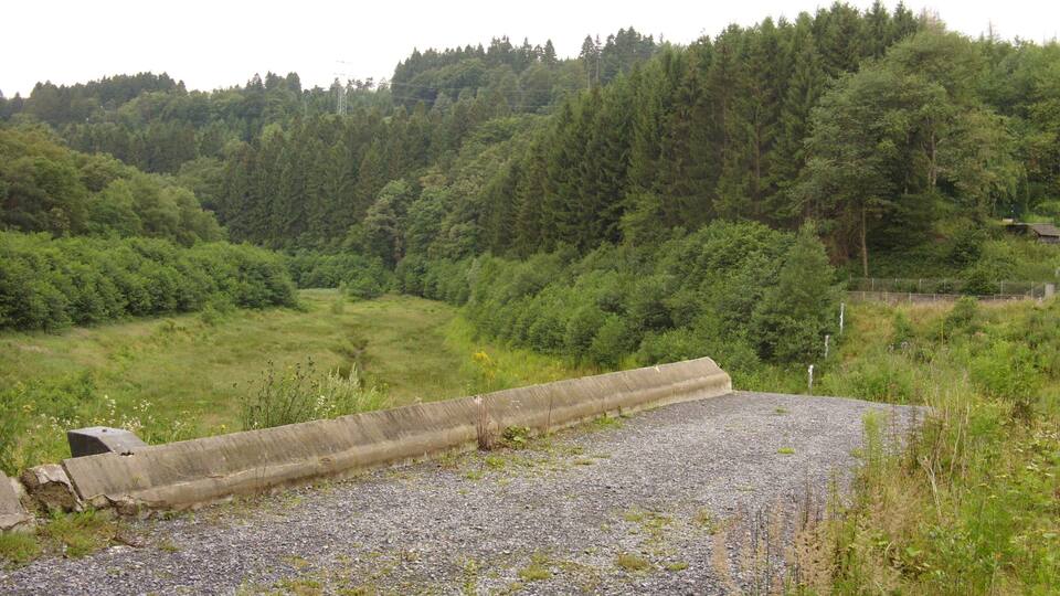A gravel path with a concrete barrier in a forested area.