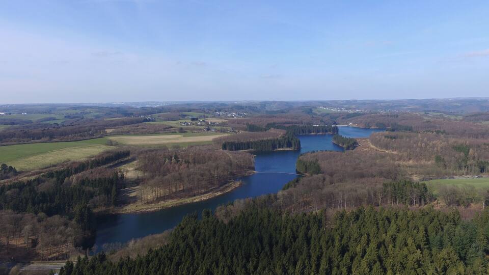 A river winding through a forested valley with fields and small buildings in the distance.