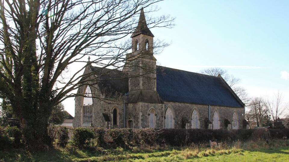 A stone church with a bell tower and a large tree in the foreground.