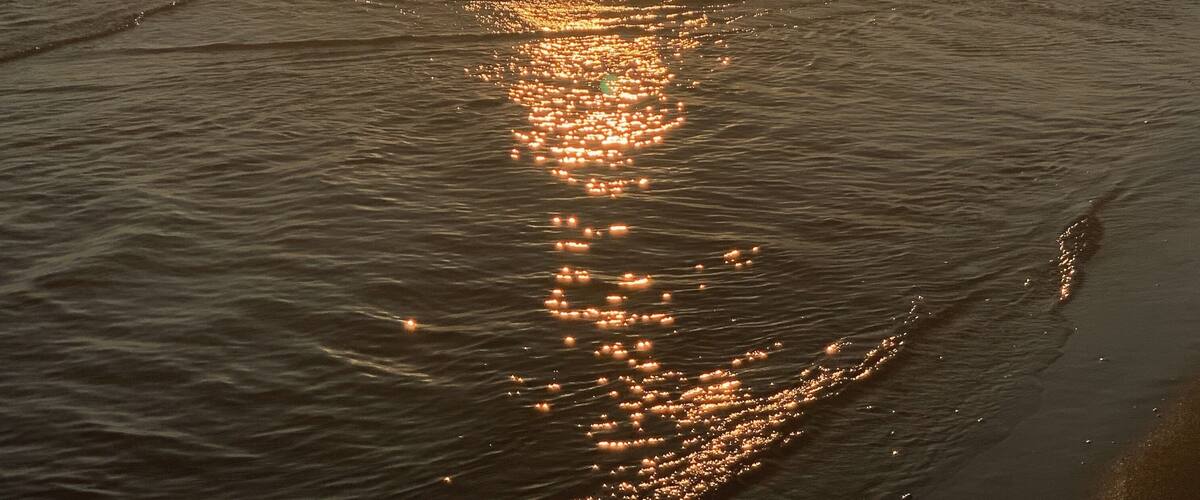 A sunset over a beach with the sun reflecting on the water.