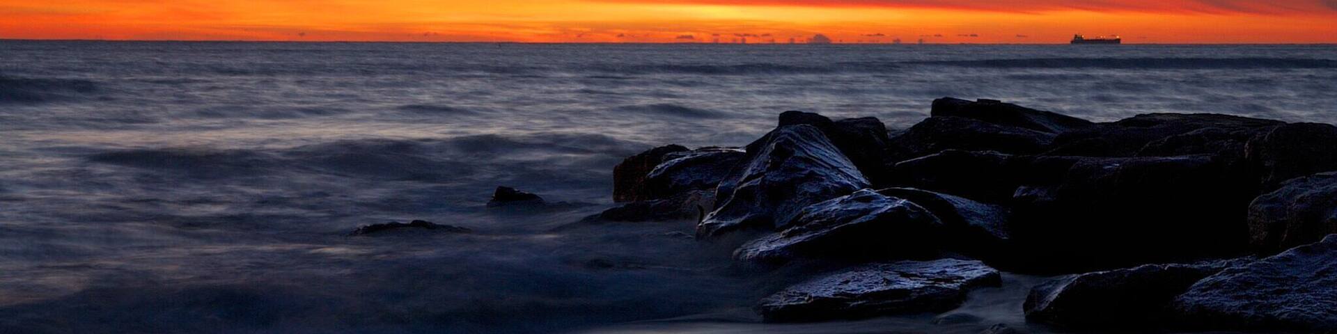 A sunset over the ocean with rocks in the foreground.