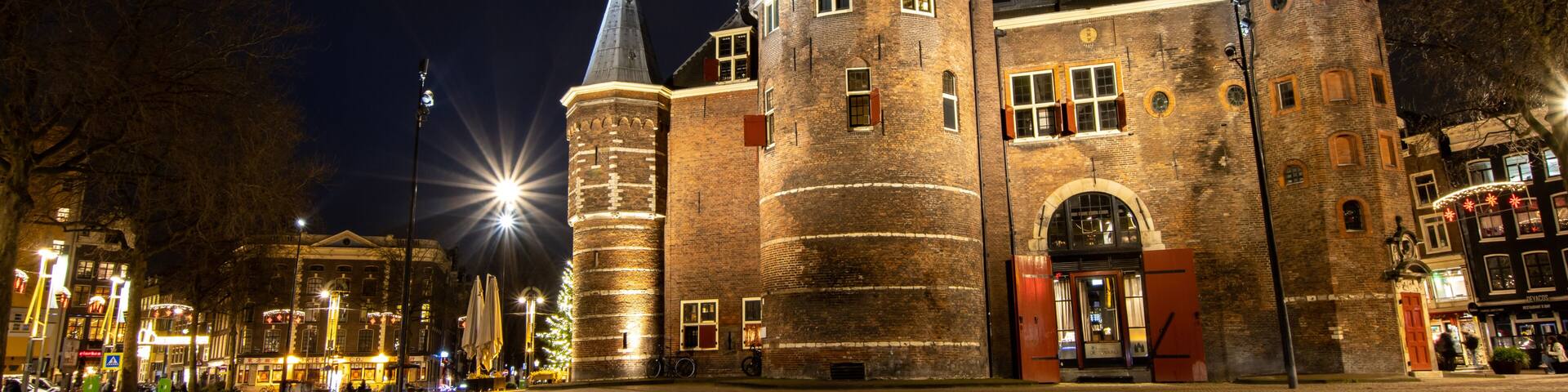A historic castle with multiple towers and a large entrance gate, surrounded by cobblestone streets and illuminated by street lamps.