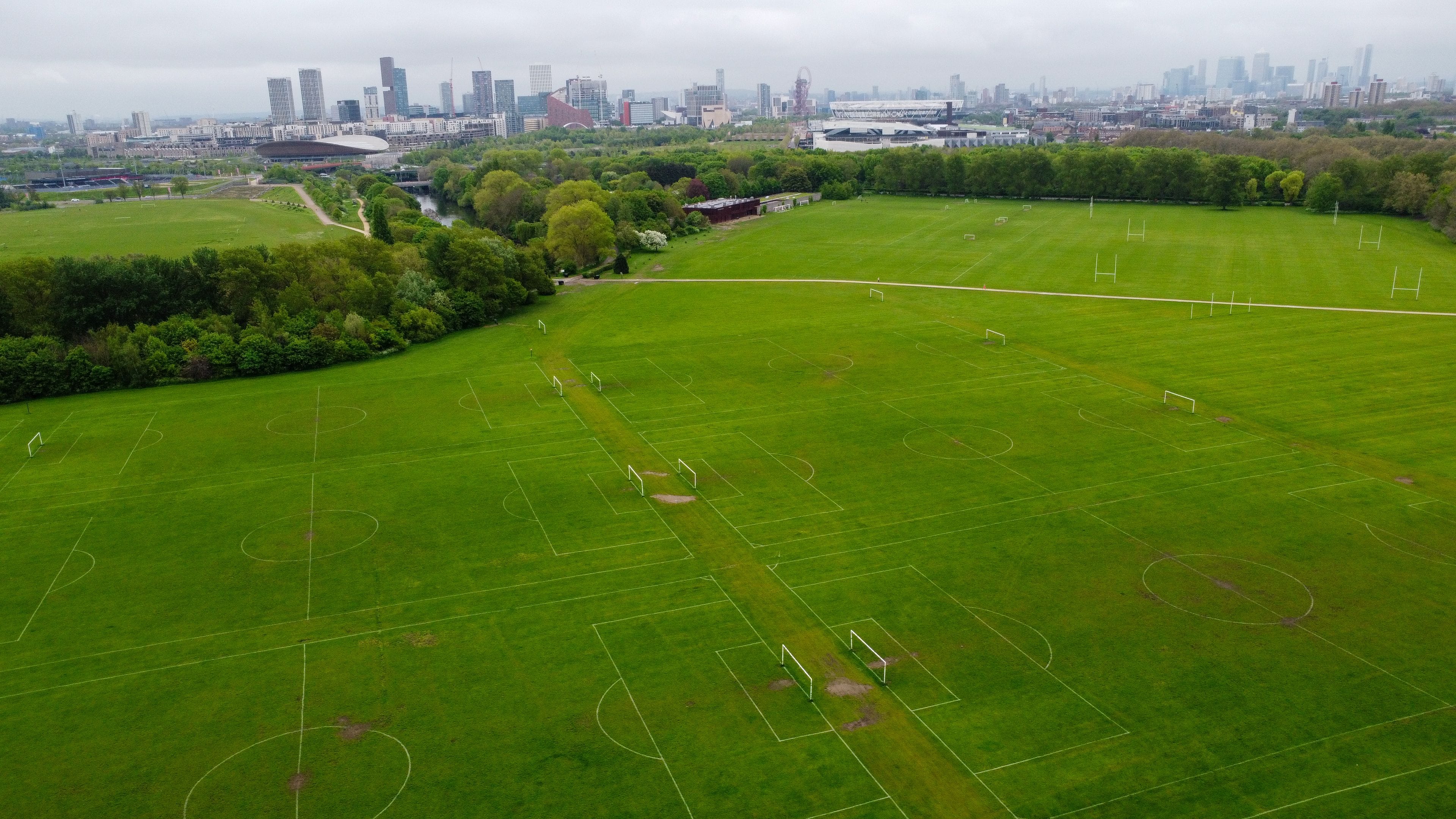 Un ampio campo da calcio verde con i pali della porta, circondato da alberi e uno skyline urbano sullo sfondo.
