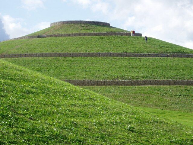 Northala Fields - main mound These people are cheating! - They are heading directly for the summit rather than following the designated path that spirals around the hill. By doing this they no doubt had to scramble over the benches that are set into the retaining wall. Moreover, they are eroding the grass which will ultimately be worn away thereby creating an ugly scar.