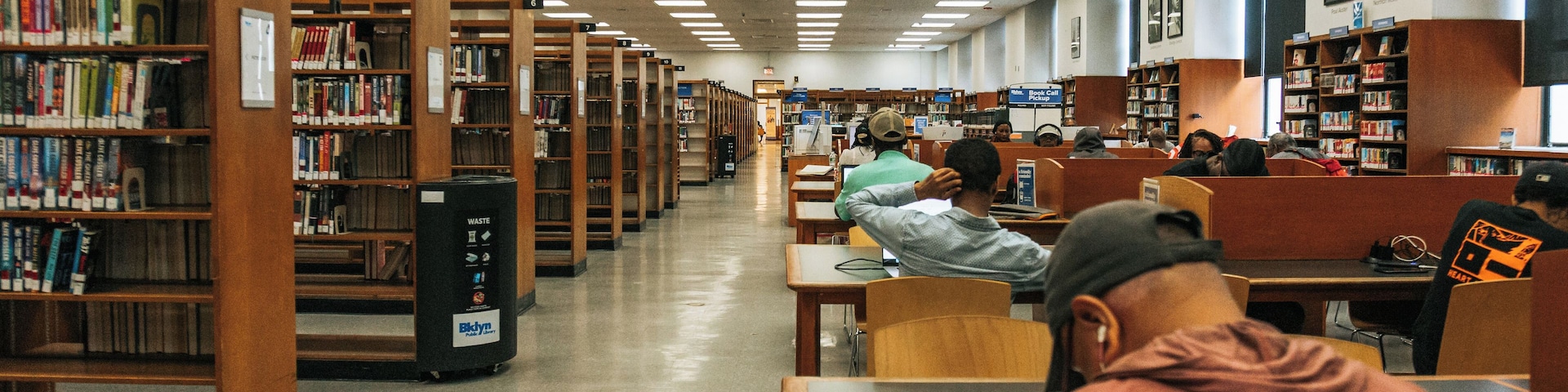 A library interior with bookshelves, reading tables, and a clock on the wall.