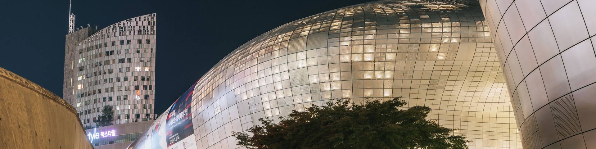 A modern architectural building with a curved glass facade and a tree in the foreground.