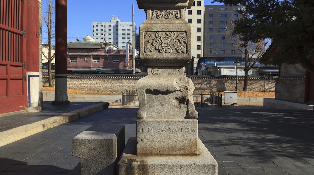 A stone monument with inscriptions, set against a backdrop of traditional architecture and modern buildings.