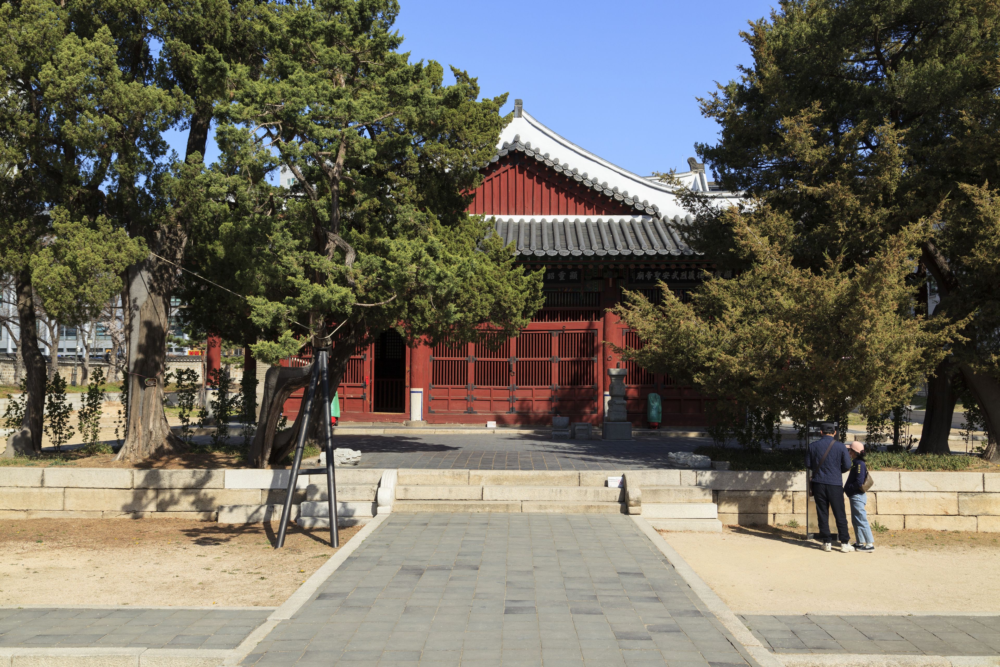A traditional Korean building with a red facade and tiled roof, surrounded by trees.