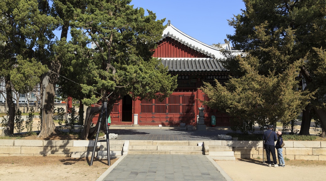A traditional Korean building with a red facade and tiled roof, surrounded by trees.