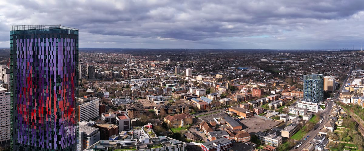 En stadsbild med en framträdande, modern byggnad med en färgstark fasad, omgiven av andra höga byggnader och en blandning av bostads- och affärsfastigheter.