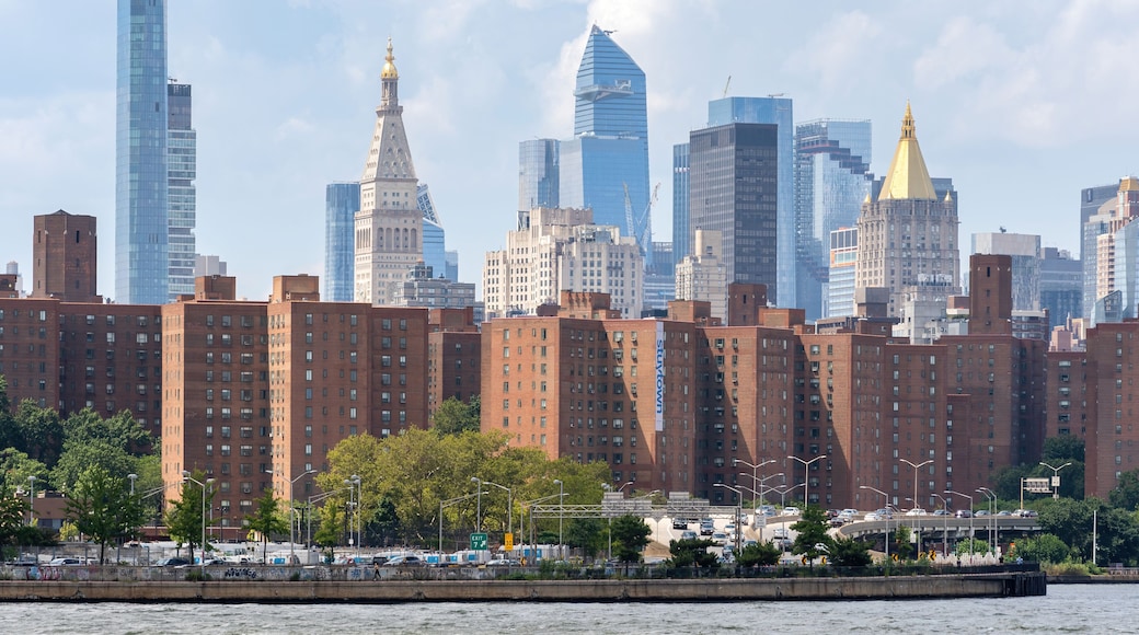 A city skyline with a mix of modern skyscrapers and historic buildings, a river in the foreground, and a clear sky.