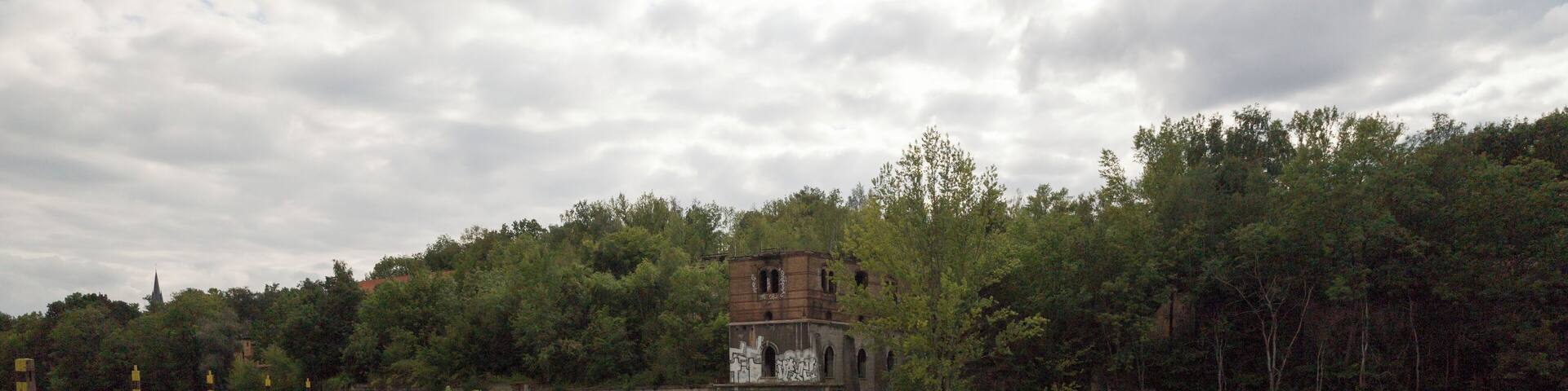 A river with a building on the opposite bank, surrounded by trees.