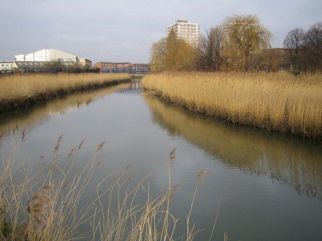River Roding in Barking Looking upstream, the footbridge in 111233 and the tower blocks in 322334 can both be seen in the distance. The reed beds visible along this reach of the river are important, and in this area, unique wildlife environments. In a couple of places the river has meandered in the past, but the meanders have subsequently silted up allowing the reeds to grow. However the organization that was responsible for building the flood defence walls has gone to great lengths to preserve the reeds by building the wall around the outskirts of the old meander line.